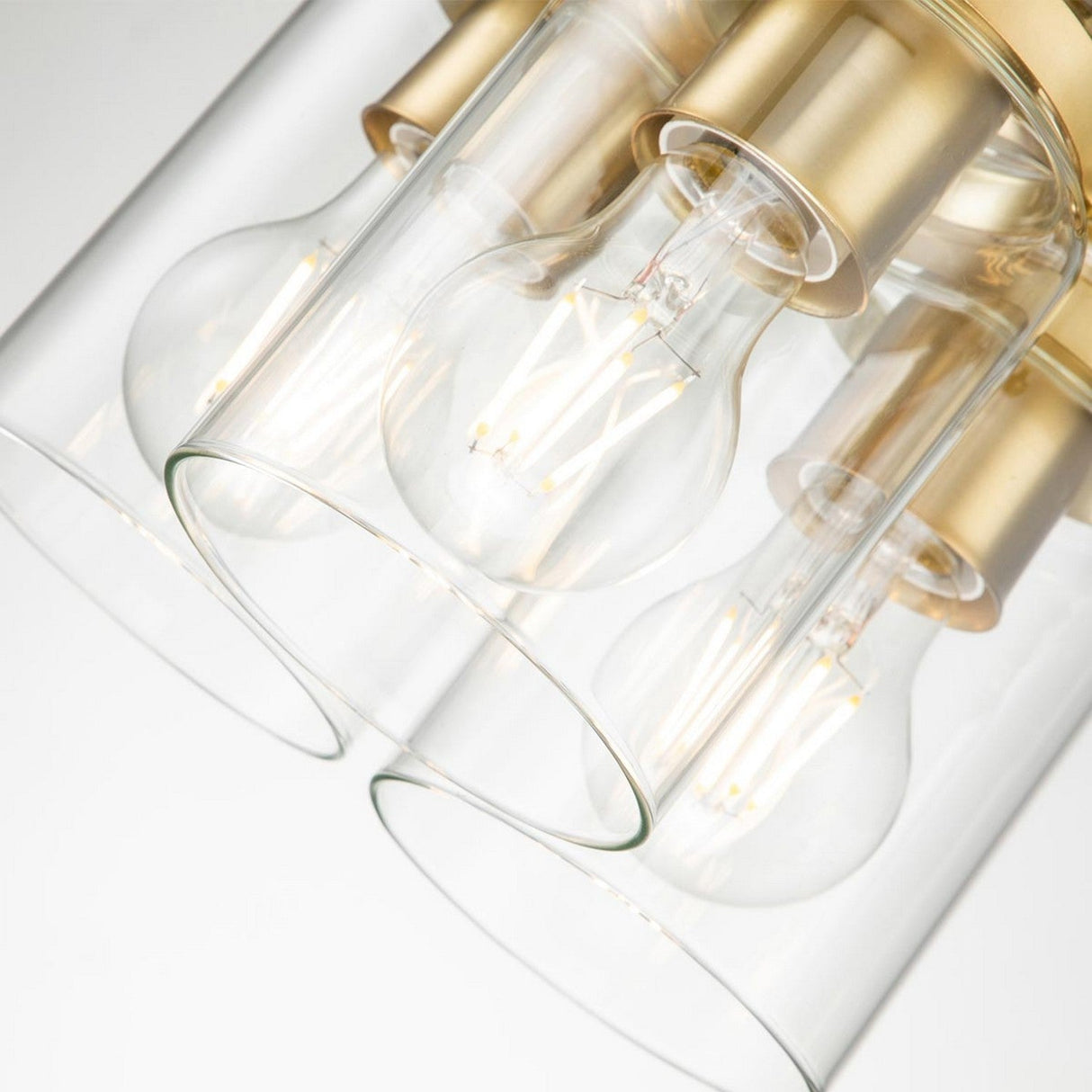 Close-up view of a contemporary ceiling light fixture with four exposed bulbs surrounded by clear glass shades, finished in brushed brass. This design captures the simplicity and elegance akin to the Brinley 3 Light Pendant - Brushed Brass.
