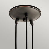The Brinley 3 Light Pendant in bronze features a round ceiling mount and three black cables that extend downward, each highlighted by clear glass shades, exuding vintage charm. The light gray background provides a perfect contrast to the dark fixture.