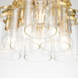 A close-up of the Brinley 6 Light Pendant showcases its exposed bulbs and cylindrical clear glass shades. The fixture's brushed brass pendant accents enhance its Mid-Century Modern vibe, featuring multiple light sources for a warm, inviting glow.