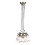 The Brinley 6 Light Pendant in brushed nickel features a modern design with a sleek metal finish. It includes six clear glass shades, each housing a bulb, which exude vintage charm. These lights are elegantly suspended by individual wires from a single circular ceiling mount.