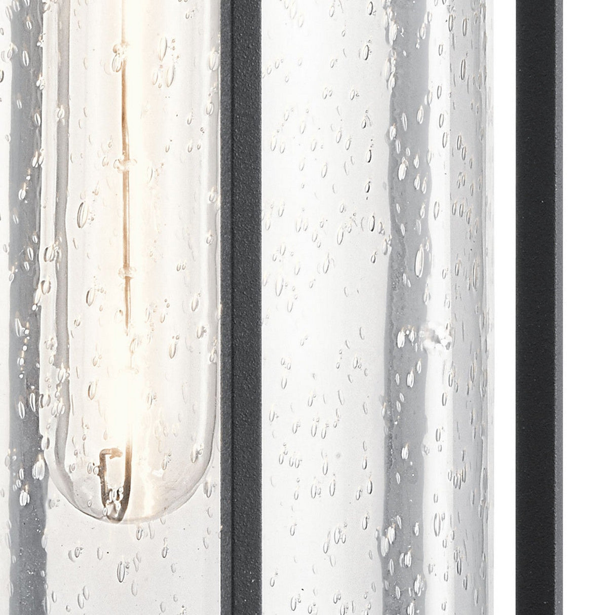 A close-up view of the Camillo Outdoor 1 Light Medium Wall Lantern - Black reveals a clear seeded glass tube adorned with water droplets. Inside, a glowing filament emits a warm glow, framed by an elegant black finish, beautifully showcasing the texture and transparency of the glass.