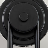 Close-up of a black metal circular wall hook with two vertical rods attached at the bottom, set against a light gray background. The minimalist design harmonizes with the Capitol Hill 2 Light Wall Light - Black, creating an elegant and cohesive look.