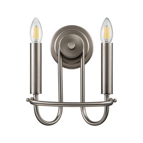 Introducing the Capitol Hill 2 Light Wall Light in Brushed Nickel, featuring a contemporary design with two cylindrical holders and exposed bulbs for a candle flame effect. This elegant sconce is mounted on a circular base with an elegantly curved metal structure.