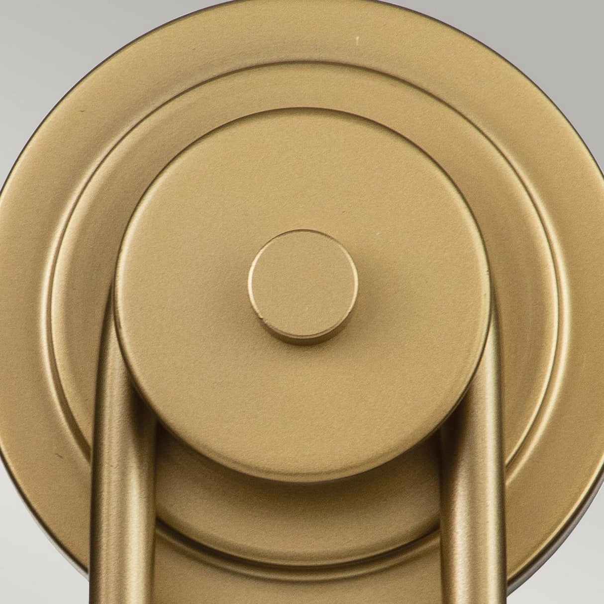 Close-up view of the Capitol Hill 2 Light Wall light in Natural Brass, featuring a gold metallic circular design with layered discs and a cylindrical pattern. The wall light resembles an elegant brass fixture against a light gray background, exuding a modern, industrial appearance that is perfect for home lighting decor.