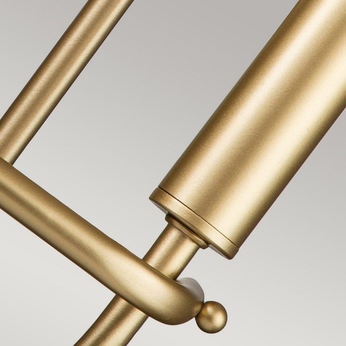 Close-up of the Capitol Hill 2 Light Wall Light in Natural Brass, showcasing its modern design with sleek cylindrical and curved elements. The elegant piece features a soft matte finish and clean lines, set against a plain gray background, making it an exceptional addition to any home lighting setup.