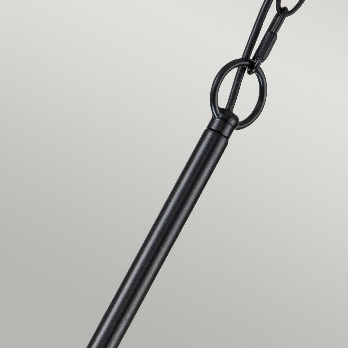 A striking close-up of the Capitol Hill 6 Light Chandelier - Black features its elegant rod attached to a ring, suspended by a chain against a light gray background. The sleek design of the chandelier rod creates a beautiful contrast with the textured links of the chain and ring.