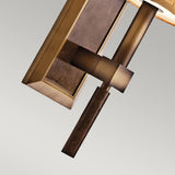 A close-up of the Celestial 1 Light Wall Light in bronze showcases its modern geometric design, featuring a vertical metal rod and rectangular mounting plate with a warm brown finish, set against a soft, neutral background.