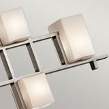 A close-up of the City Lights 7 Light Linear Chandelier in silver showcases its sleek and geometric design, complemented by white frosted square lampshades. The integrated LED lights are stylishly organized on a metallic grid structure, enhancing the modern decor of the room with a contemporary flair.