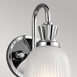 The Cora 1 Light Wall Light - Polished Chrome is a modern bathroom wall sconce that boasts a polished chrome finish with a fluted design and an IP44 rating. It is mounted on a circular base and features a ribbed glass shade, bringing a sleek and elegant touch to any room.