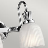 A close-up of the Cora 2 Light Wall Light in polished chrome features a modern wall-mounted fixture with a curved arm and a ribbed frosted glass shade, compatible with LED bulbs, set against a neutral gray background—ideal for bathroom lighting.