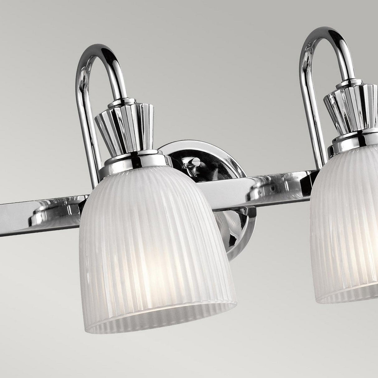 A detailed view of the Cora 4 Light Wall Light in polished chrome, showcasing its LED lamps with two frosted glass shades against a gray backdrop.