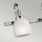 The Cora 4 Light Wall Light in polished chrome showcases a contemporary curved design, ideal for bathroom lighting. Its vertical ribbed glass shade diffuses a gentle light from LED lamps, all elegantly mounted on a rectangular base.