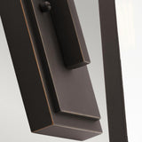 Close-up of the Delison Outdoor 1 Light Wall Lantern in rubbed bronze against a muted background, seamlessly blending with the rustic lodge exterior. Its sleek and minimalist rectangular design features slightly rounded edges, creating a harmonious look.