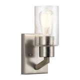 Deryn 1 Light Wall Light in Antique Grey features a brushed metal base and a cylindrical clear seeded glass shade. The exposed bulb enhances the textured glass, blending modern and industrial styles with rustic elegance.