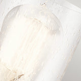 A detailed view of the Deryn 1 Light Wall Light in Antique Grey reveals a lit bulb inside a glass enclosure adorned with water droplets, producing a diffused and soft glow. This image captures rustic elegance through its tranquil and calming ambiance, accentuated by how the light interacts with the clear seeded glass.