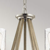 A close-up of the Deryn 5 Light Chandelier in antique grey showcases its modern design with a brushed nickel finish and rustic charm. Wooden beams converge at the top, with two speckled-textured glass shades partially visible below, complemented by accents of antique grey.