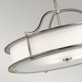The Emory 4 Light Duo-Mount Chandelier - Silver features a sleek, silver finish with a brushed metal frame encircling its white cylindrical shade. The fixture is elegantly suspended by a metallic rod against a neutral gray backdrop.