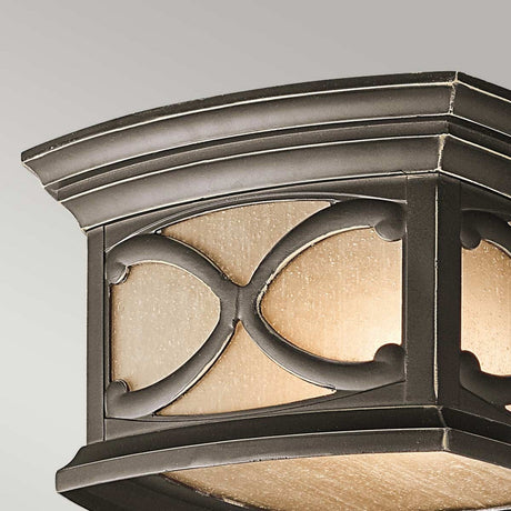 The Franceasi Outdoor 2 Light Flush in Olde Bronze features a square ceiling light fixture with a decorative curved cross design on the metal frame. It includes amber-tinted glass panels that cast a warm glow, enhancing the elegance of this outdoor flush mount model against a neutral backdrop.