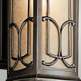 A detailed view of the Franceasi Outdoor 1 Light Medium Wall Lantern reveals its amber-tinted glass panels and elaborate black metal scrollwork. The gentle illumination from within casts a warm glow that accentuates the textured glass and graceful design, making it an ideal choice for adding charm with its olde bronze finish.