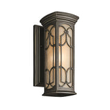 The Franceasi Outdoor 1 Light Small Wall Lantern in Olde Bronze features a rectangular design with decorative metal accents and amber-tinted glass panels, softly lighting up the area.