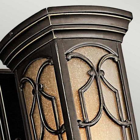 A close-up of the Franceasi Outdoor 1 Light Small Wall Lantern, showcasing an ornate vintage-style design with a decorative metal frame in Olde Bronze and frosted glass panels. The lantern features curved lines and arch patterns, offering an elegant and classic look reminiscent of traditional outdoor wall sconces. The background is simple and light-colored.