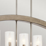 A close-up of the Grand Bank 5 Light Chandelier in antique grey showcases its gracefully curved metal frame and multiple cylindrical glass shades. The shades encase glowing light bulbs, with visible wires extending upward. The neutral light gray background perfectly highlights its timeless elegance.