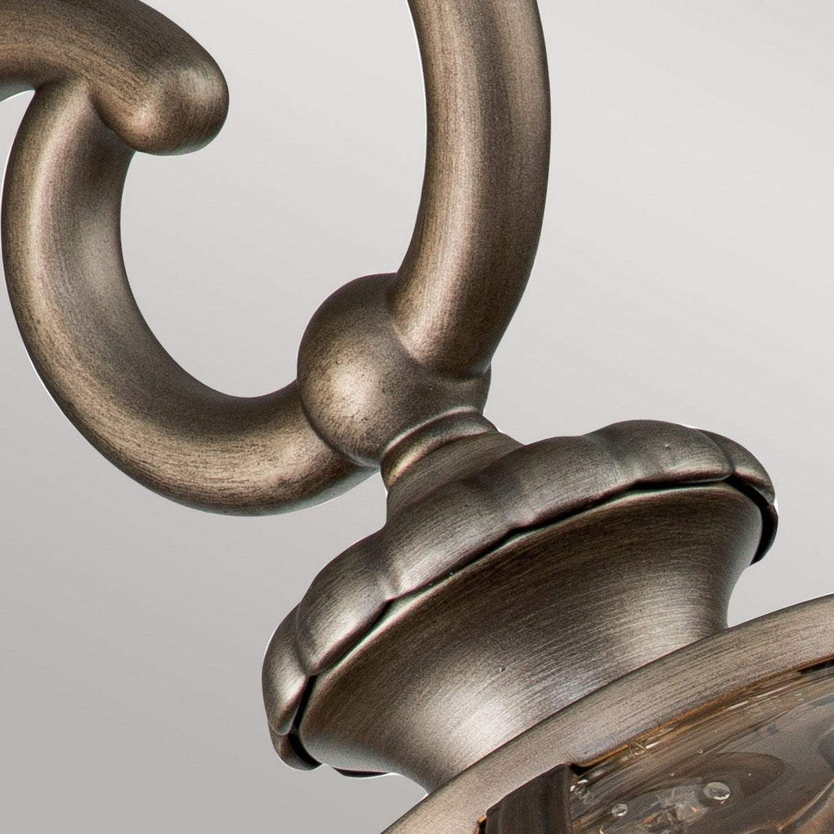 Close-up of a burnished bronze light fixture featuring a curved handle and ornamental detailing. The Halleron Outdoor 3 Light Wall Lantern, reminiscent of Victorian elegance, boasts a rich finish, highlighting its intricate design against a neutral background.