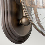 A detailed view of the Halleron Outdoor 3 Light Wall Lantern reveals its oval, burnished bronze backplate and clear, speckled glass shade. This fixture embodies Victorian elegance, featuring a design that encloses bulbs within the glass—a perfect choice for outdoor lighting.