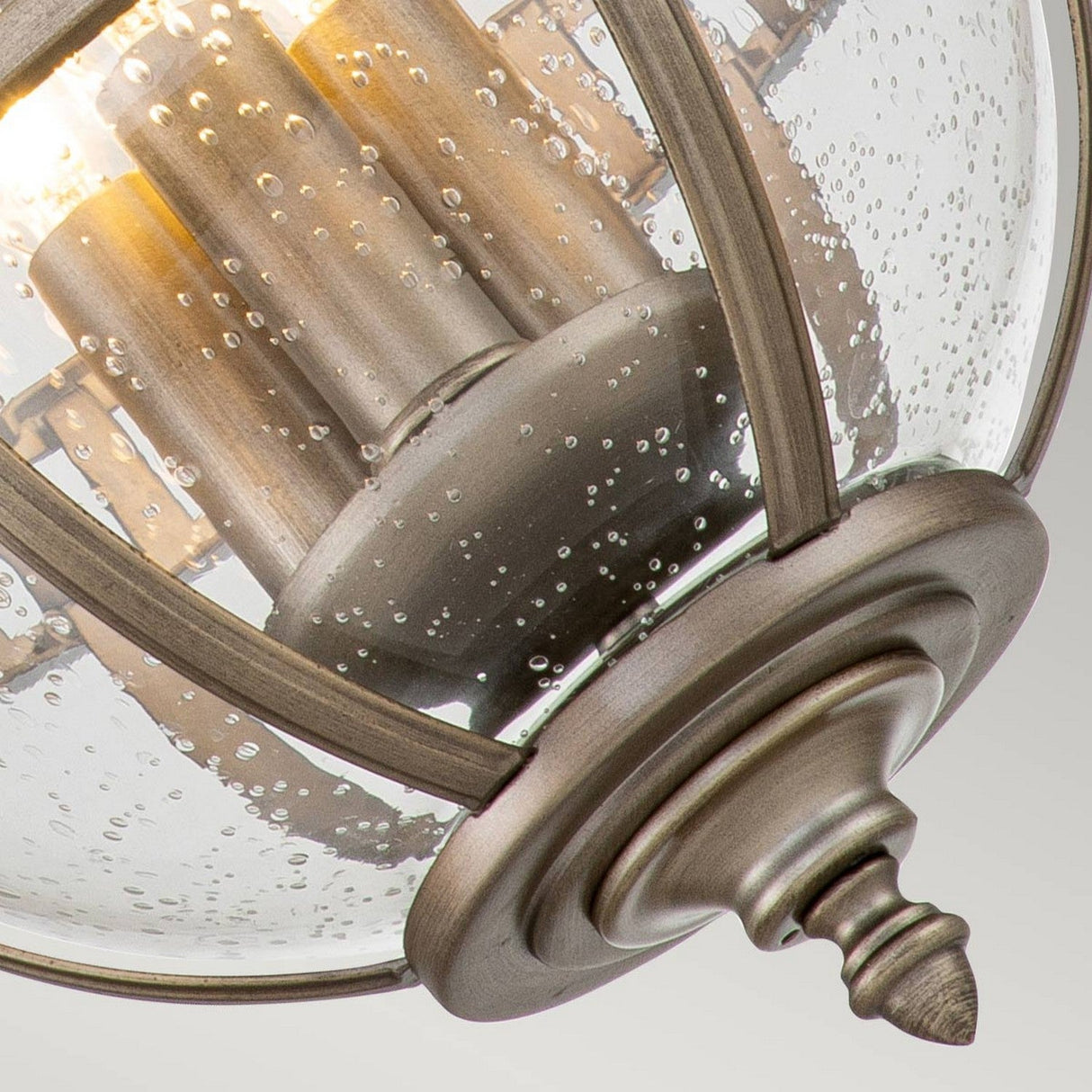 Close-up of the Halleron Outdoor 3 Light Chain Pendant featuring a Victorian-inspired design with decorative metal and bubbled glass. The burnished bronze finish reveals softly illuminated candle-style lights inside, adding an elegant touch to the outdoor fixture.