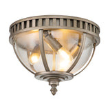 The Halleron Outdoor 3 Light Ceiling Flush in Burnished Bronze boasts a vintage-style design, showcasing a clear glass dome that elegantly reveals two glowing light bulbs within. The fixture features a decorative finial at the bottom and includes a ring with vertical slits around the top, subtly inspired by Victorian-style design elements.
