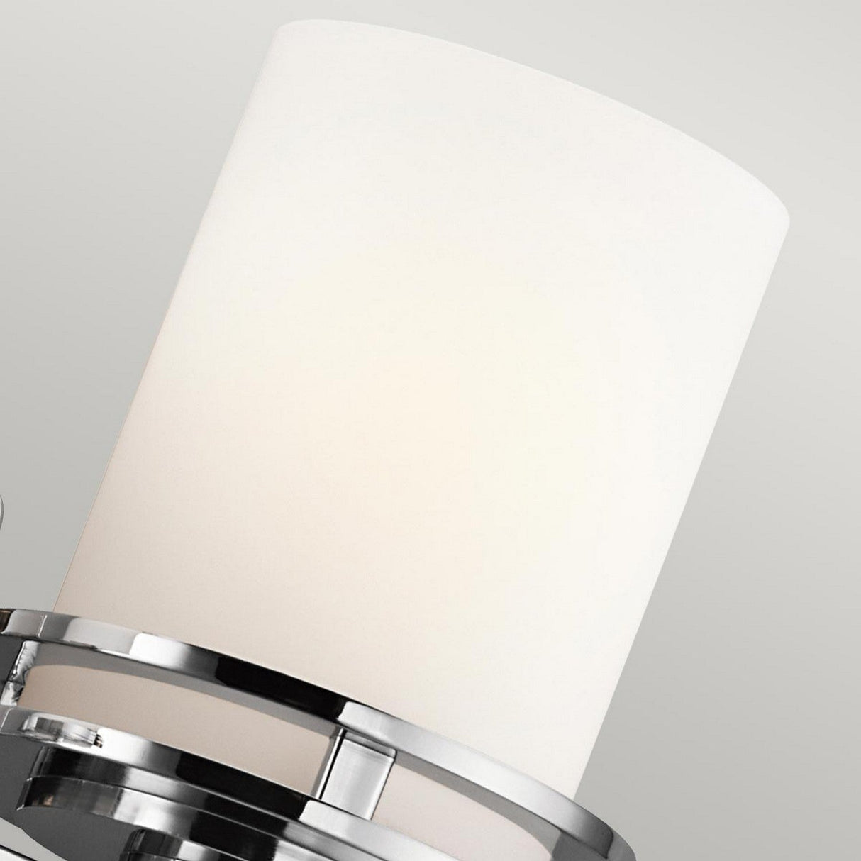 The Hendrik 2 Light Wall Light in polished chrome features a close-up view with a cylindrical white shade and sleek metal accents. This design radiates contemporary elegance, highlighted by polished chrome rings at the base of the shade, making it perfect for modern bathroom lighting against a plain, light gray background.