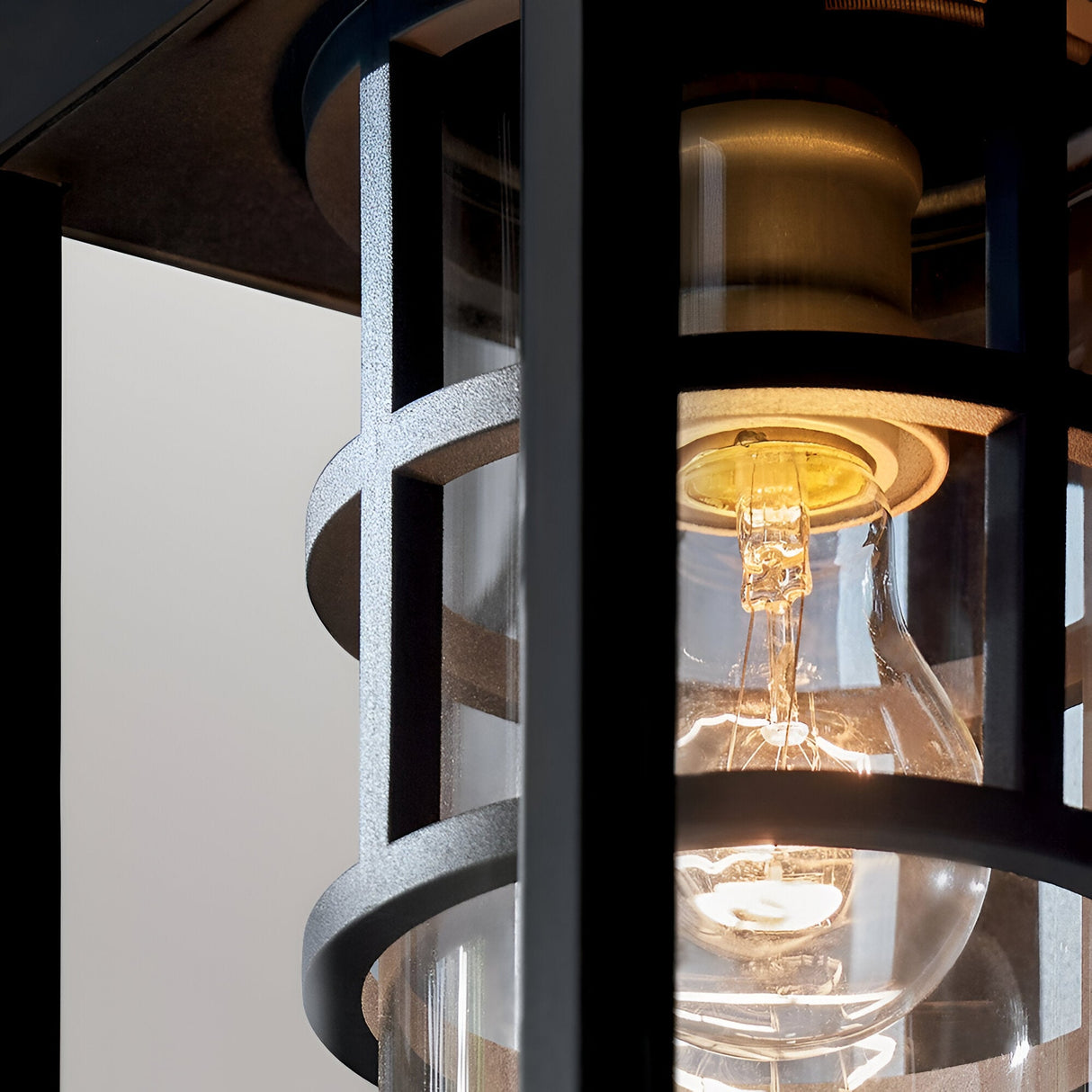 Close-up of the glowing Hone Coastal 1 Light Medium Outdoor Wall Lantern in black, featuring geometric lines and reflections on its weather-resistant glass.