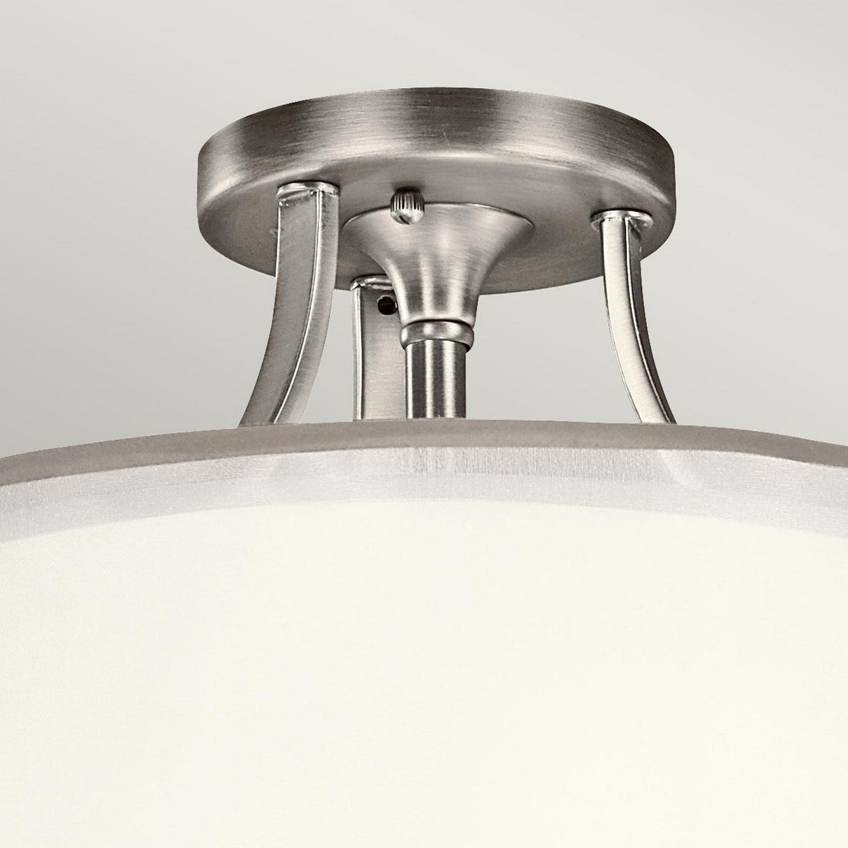 Here is a rewritten sentence based on the provided product data:

A detailed view of the Lacey 3 Light Small Semi Flush in silver, showcasing its polished finish and cylindrical white shade. It's affixed to the ceiling with sleek metallic arms, producing a layered glow effect.
