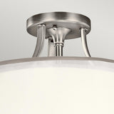 Here is a rewritten sentence based on the provided product data:

A detailed view of the Lacey 3 Light Small Semi Flush in silver, showcasing its polished finish and cylindrical white shade. It's affixed to the ceiling with sleek metallic arms, producing a layered glow effect.
