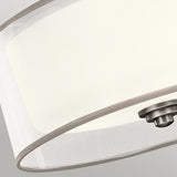 Close-up of the Lacey 3 Light Small Semi Flush - Silver ceiling light fixture, featuring a round, translucent white shade and a polished silver finish. The image emphasizes the lower part, showcasing its minimalistic and sleek design with a layered glow against a neutral background.
