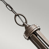 Close-up of the Lacey 5 Light Chandelier - Bronze, hanging from a chain against a neutral background. The chandelier features a bronze finish with geometric design elements, reminiscent of transitional interiors, attached to a cable with a circular ring.