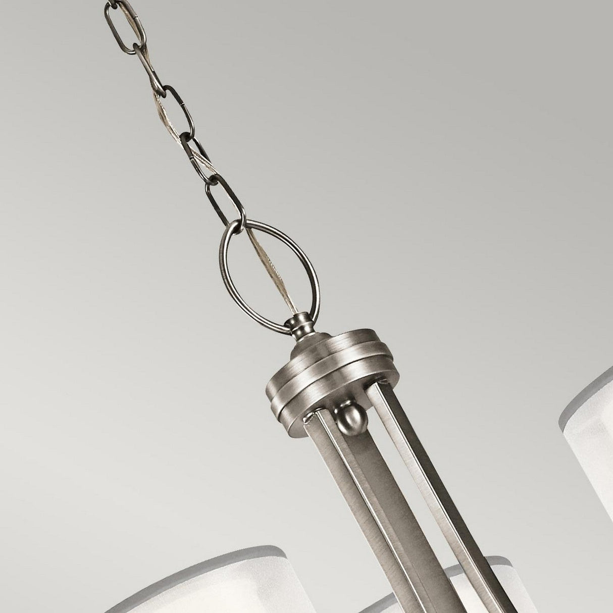 A close-up view of the Lacey 9 Light Chandelier - Silver hanging from a chain showcases its sleek metallic design with partially visible cylindrical frosted glass shades, set against a neutral background.