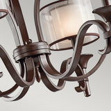 Close-up of the Lacey 9 Light Chandelier - Bronze, showcasing its ornate double-shade design with elegantly curved metal arms and frosted glass shades, each illuminated by a bulb, set against a plain gray background.
