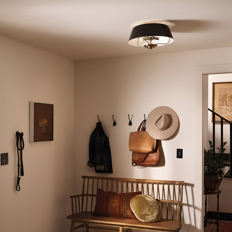 A welcoming entryway features a wooden bench topped with cushions, wall hooks for hanging items such as hats and bags, and the Luella 3 Light Duo-Mount Chandelier/Semi-Flush in Black & Brass casting a gentle glow. The black and brass details perfectly complement the framed art on the walls.