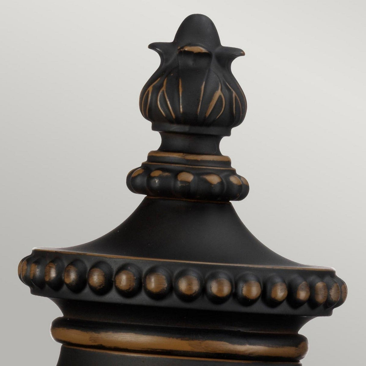 Close-up of the Luverne Outdoor 1 Light Medium Pedestal in rubbed bronze, showcasing its floral-like design at the top and intricate detailing on the body, set against a plain light gray background.