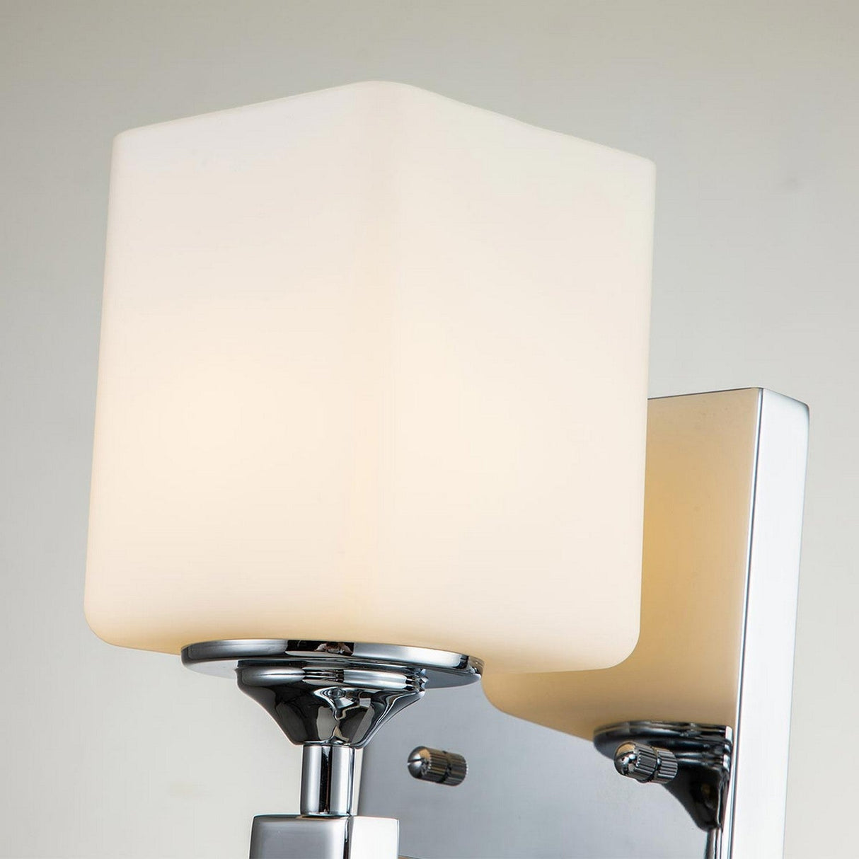 The Marette 1 Light Wall Light in Polished Chrome features a sleek design with a square opal glass shade, casting a soft, warm glow against a light-colored wall.