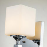 The Marette 1 Light Wall Light in Polished Chrome features a sleek design with a square opal glass shade, casting a soft, warm glow against a light-colored wall.