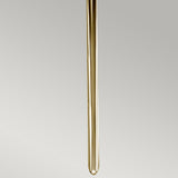A long transparent glass tube, narrow and cylindrical in shape, hangs vertically against a neutral gray background, mirroring the Mid-Century Design of the Mona 2 Light Large Wall Light in Polished Brass. Its elegance is highlighted by understated touches of polished brass.