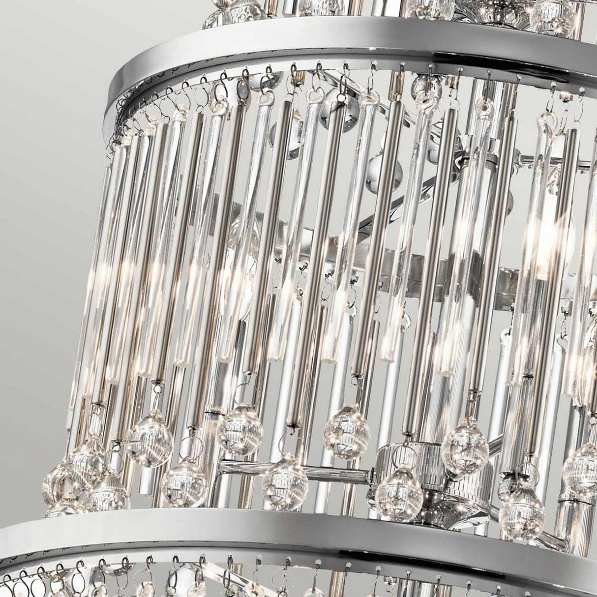 A close-up of the Piper 18 Light Chandelier in polished chrome showcases its elegant design, featuring multiple layers of hanging crystal rods and clear glass bead accents. Its frame beautifully reflects light, enhancing the chandelier's allure.