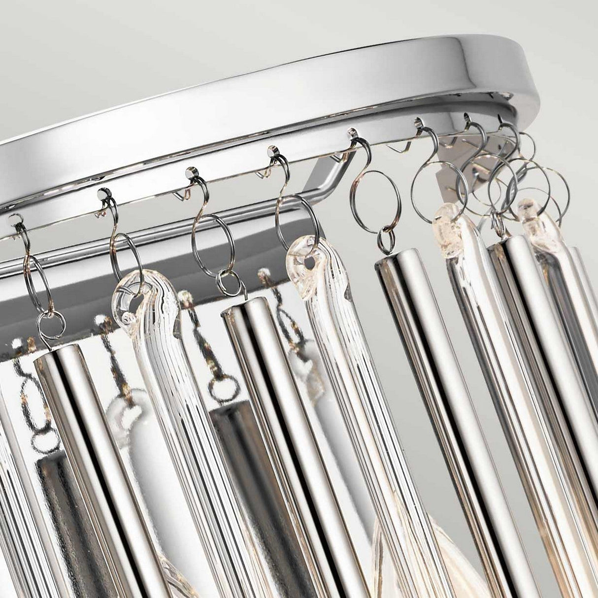 Close-up of the Piper 2 Light Wall Light in polished chrome, featuring multiple clear, cylindrical glass rods hanging vertically. The sleek design reflects light and exudes contemporary elegance, making it a perfect complement to any space alongside a modern chandelier.