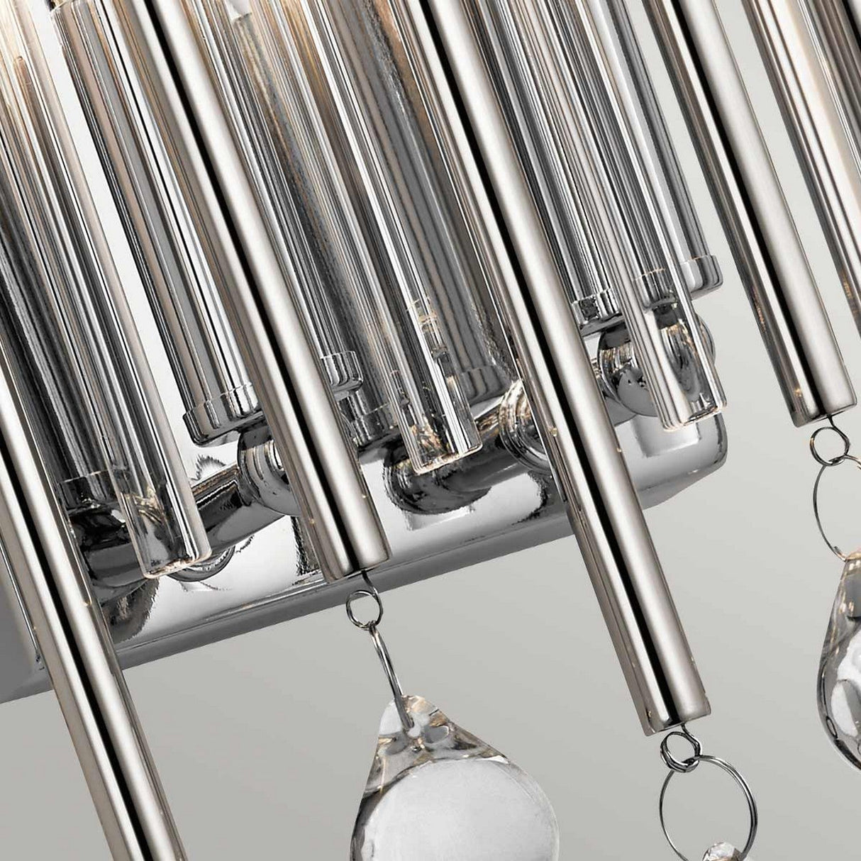 Close-up of a contemporary chandelier featuring vertical metallic rods in polished chrome and hanging crystal pendants. The rods form a sleek, linear design, while the crystals elegantly reflect light. It is ideal for complementing the Piper 2 Light Wall Light - Polished Chrome or pairing with another sophisticated wall light.