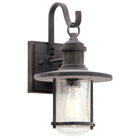 The Riverwood Outdoor 1 Light Medium Wall Lantern - Weathered Zinc exudes rustic elegance with its weathered zinc frame and curved top. Enclosed in clear, textured glass, the visible bulb imparts a vintage charm, making it a perfect choice for exterior lighting.