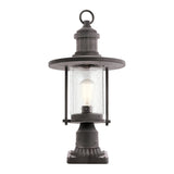 The Riverwood Outdoor 1 Light Pedestal Lantern in weathered zinc features a black nautical-inspired vintage design. It includes a circular top and clear glass housing that encloses an exposed light bulb, all resting on a square base ideal for outdoor use.
