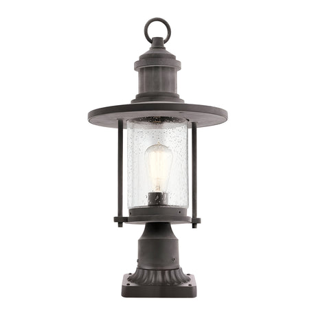 The Riverwood Outdoor 1 Light Pedestal Lantern in weathered zinc features a black nautical-inspired vintage design. It includes a circular top and clear glass housing that encloses an exposed light bulb, all resting on a square base ideal for outdoor use.
