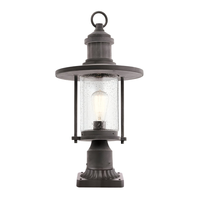 The Riverwood Outdoor 1 Light Pedestal Lantern in weathered zinc features a black nautical-inspired vintage design. It includes a circular top and clear glass housing that encloses an exposed light bulb, all resting on a square base ideal for outdoor use.
